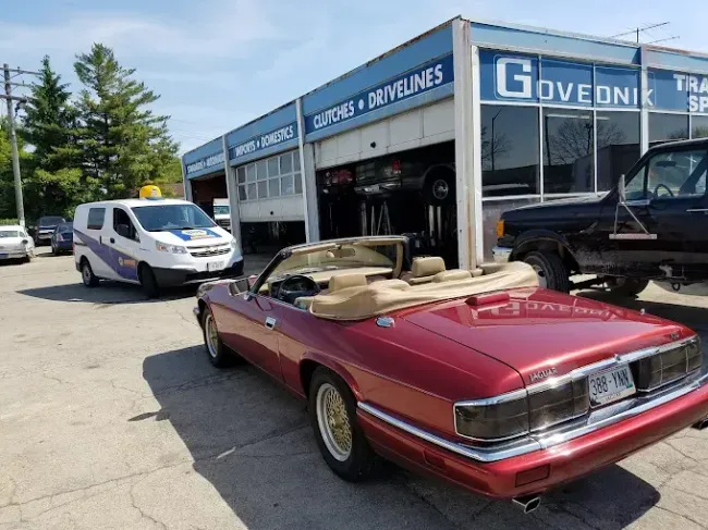 Red convertible parked outside an auto repair shop, with a white van nearby.