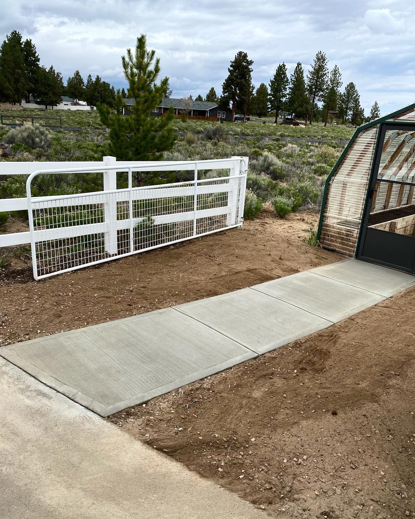 A walkway leading to a greenhouse with a white fence in the background.