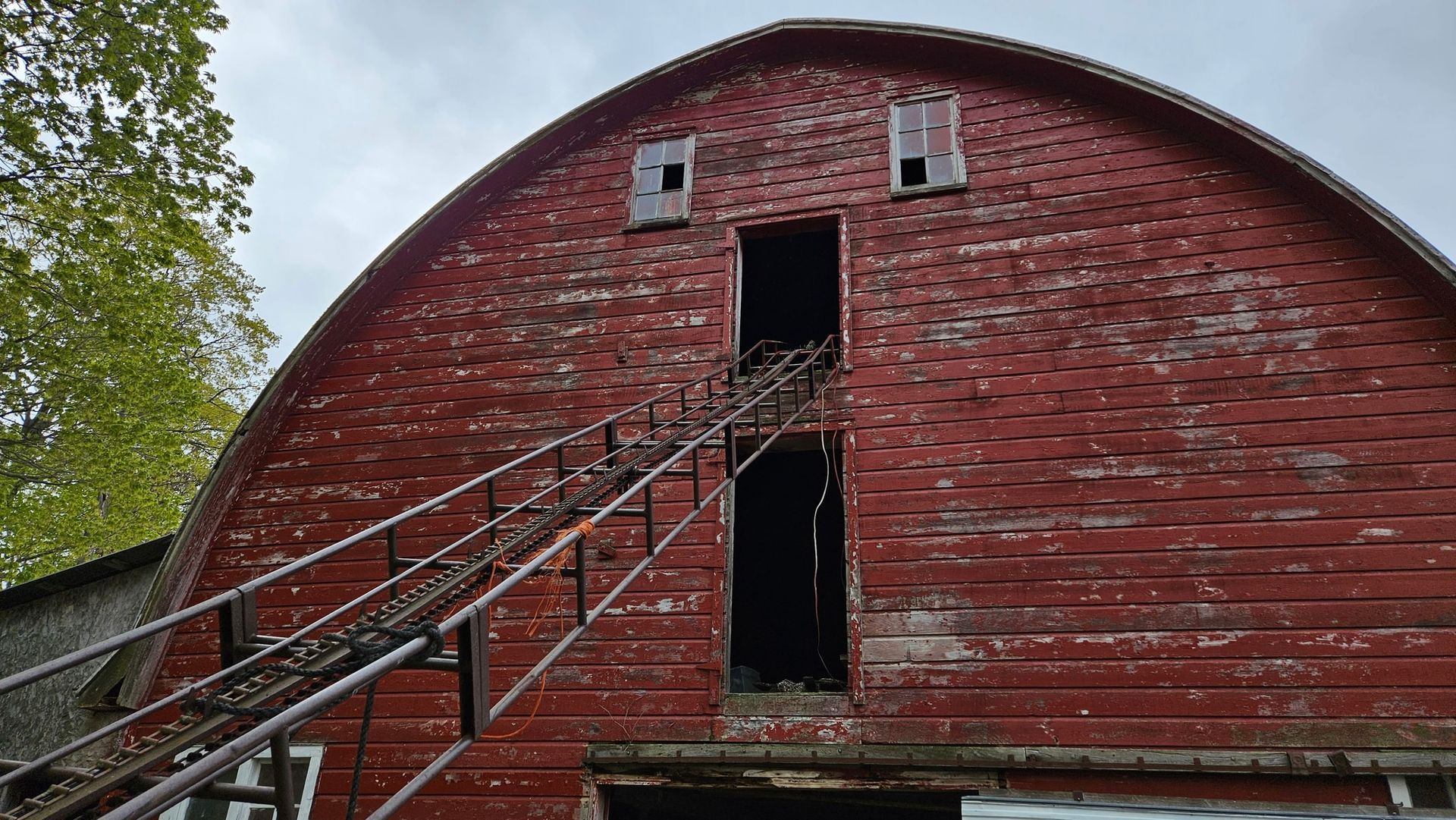 Red barn with arched roof, weathered wood, open door, ladder, cloudy sky.