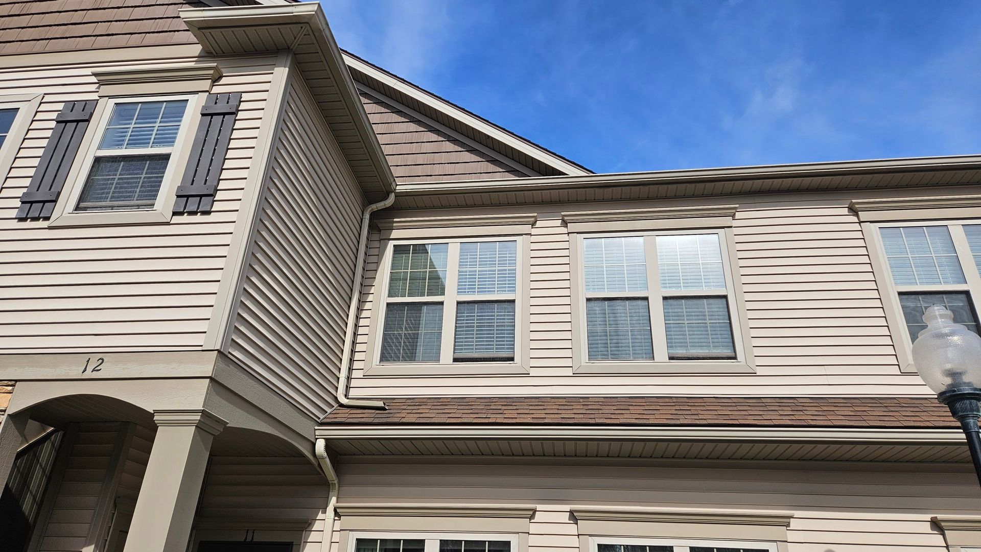 Townhouse exterior with beige siding, brown trim and shutters, windows under a blue sky.