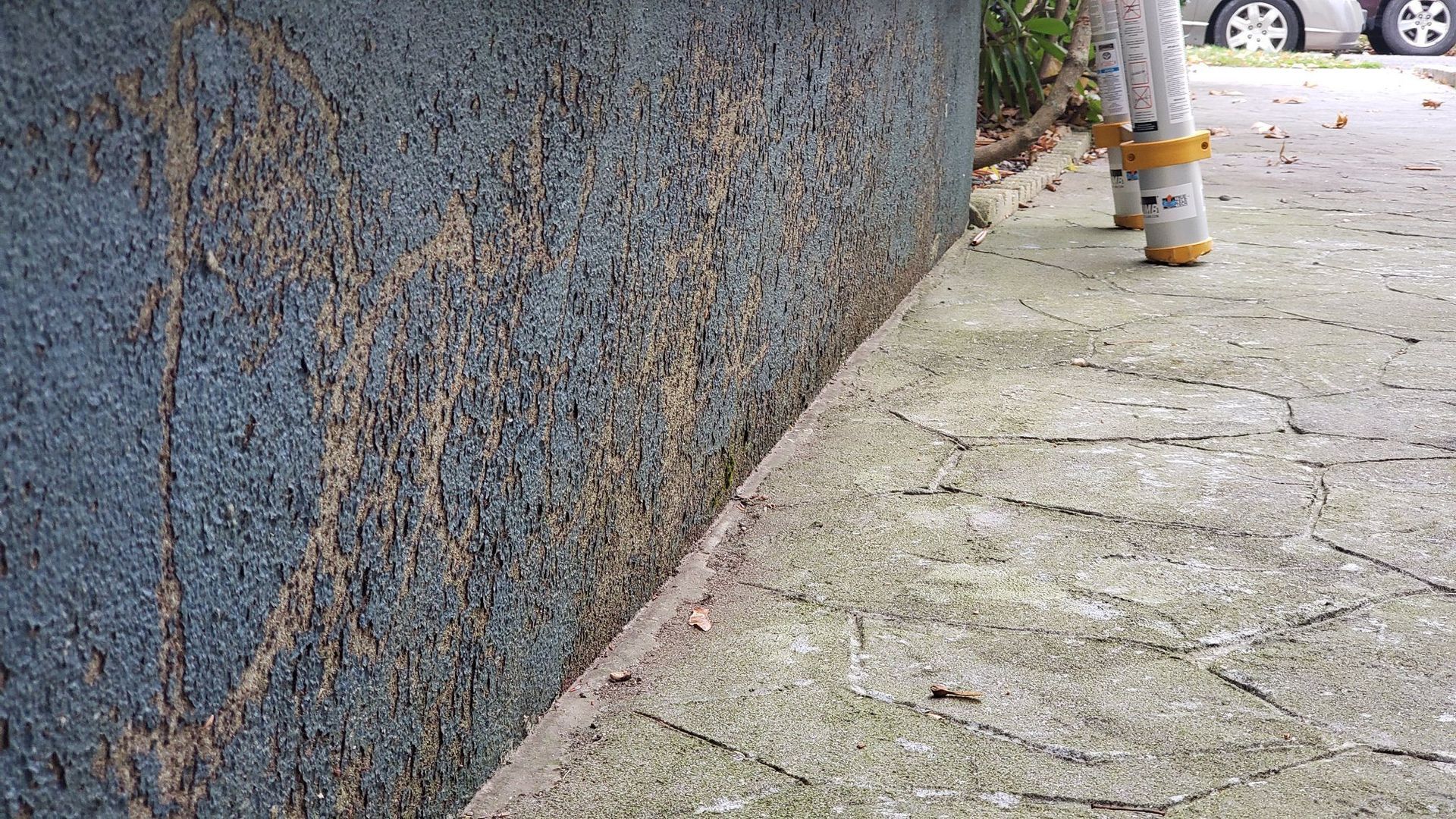 Blue textured wall with brown streaks next to a concrete path.