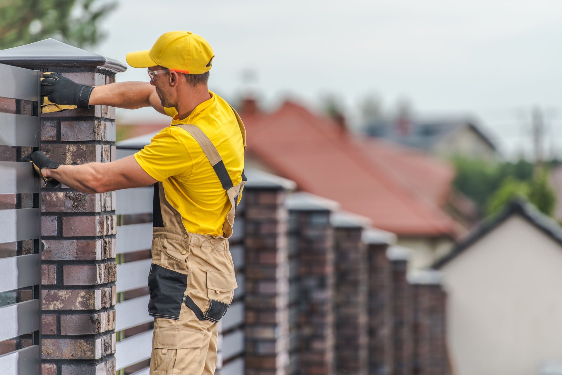 A construction worker in yellow shirt and cap building a brick fence.
