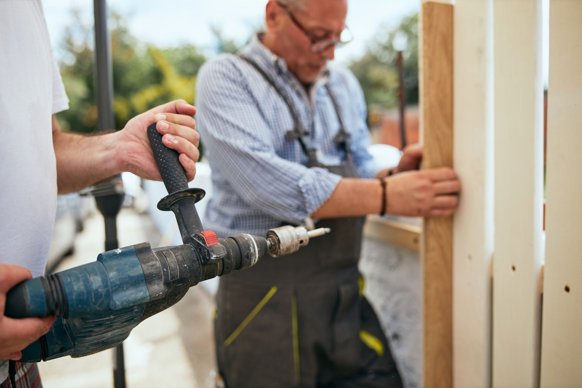 Two skilled male construction workers installing a wooden fence with an electric drill.
