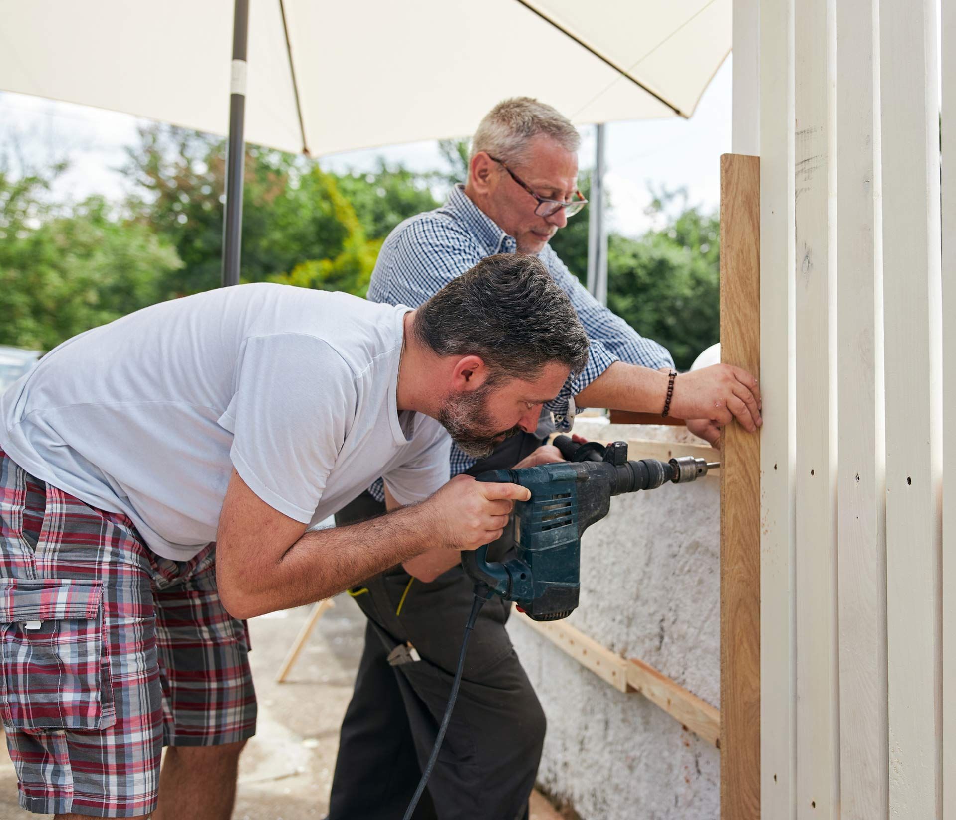 Two men performing custom fence installation using a power drill and wooden panels.
