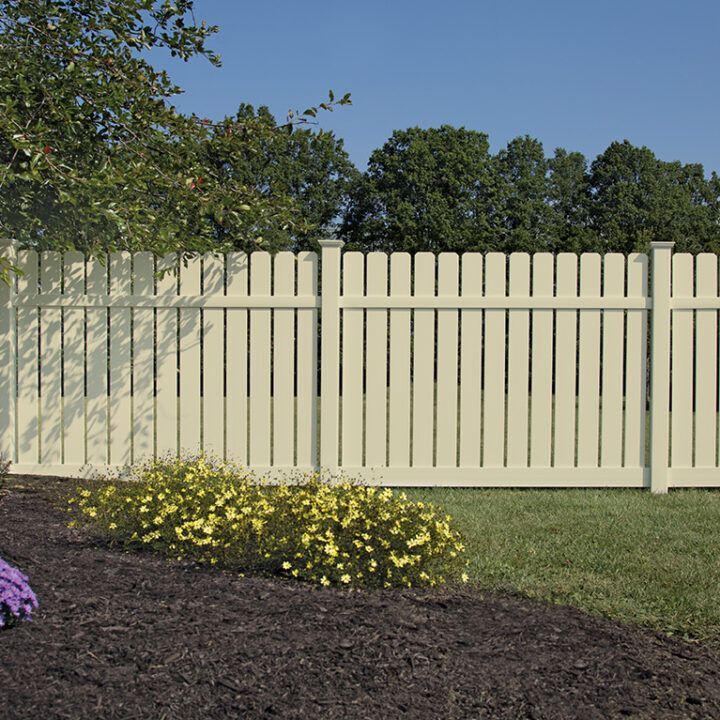 A wooden fence surrounds a grassy area in front of a house.