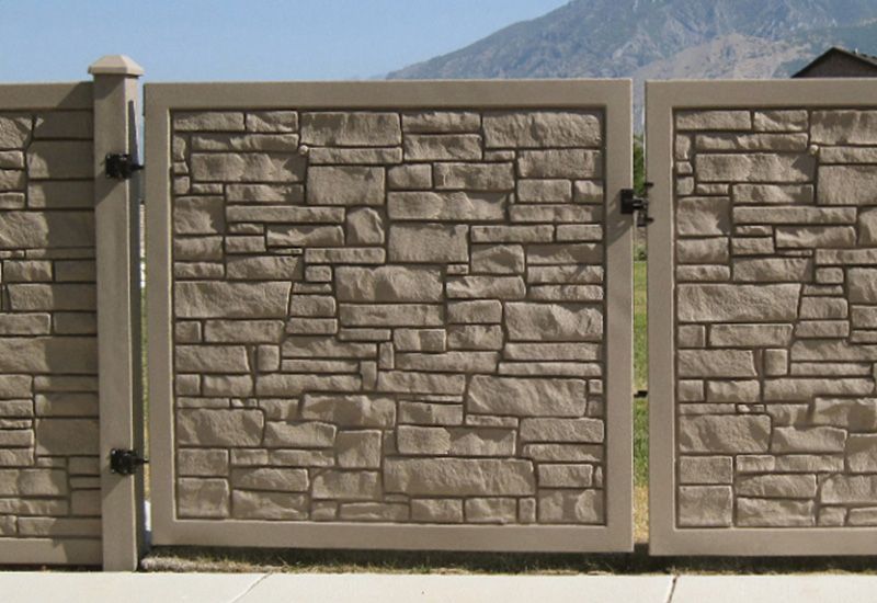 Stone-patterned tan gate and fence with a mountain backdrop.