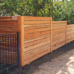 Fence With A Metal Gate Is Surrounded By Trees — Warren, MI — Kimberly Fence & Supply