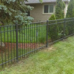 Metal Fence Surrounds A Lush Green Yard In Front Of A House — Warren, MI — Kimberly Fence & Supply