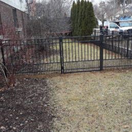 Metal Fence Surrounds A Grassy Yard In Front Of A Brick Building — Warren, MI — Kimberly Fence & Supply