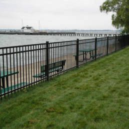 Black Fence Surrounds A Grassy Area Next To A Body Of Water — Warren, MI — Kimberly Fence & Supply