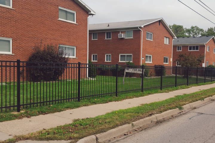 Black Fence Surrounds A Brick Apartment Building Next To A Sidewalk — Warren, MI — Kimberly Fence & Supply