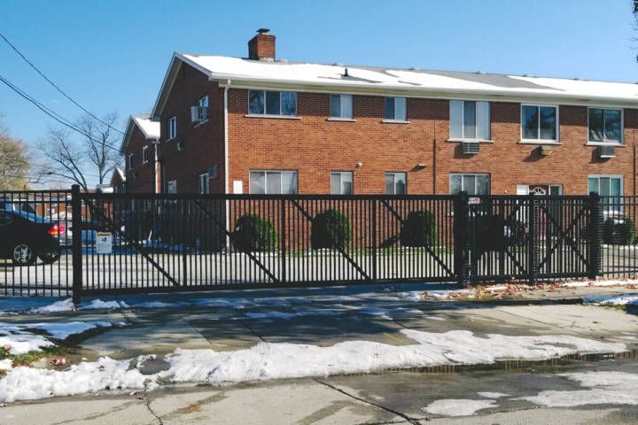 Black gate in front of red brick apartment building on a sunny day; remnants of snow on the ground.