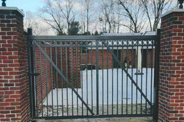 Black metal gate between brick pillars, leading to a courtyard covered in snow.
