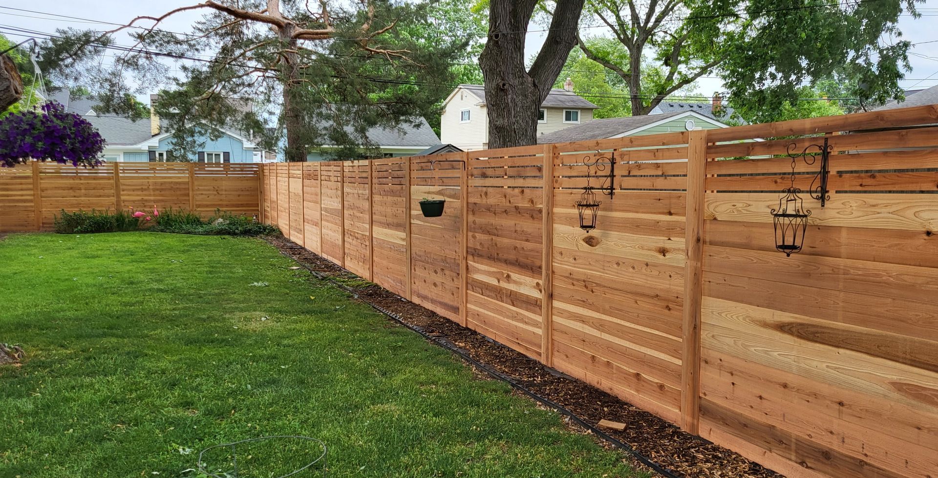 A wooden fence surrounds a green lawn. Bird feeders hang on the fence.