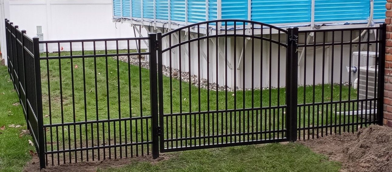Black wrought iron fence with a gate enclosing a green area of grass.