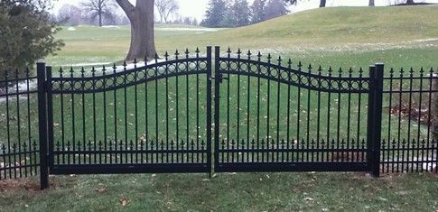 Black wrought iron gate and fence in a grassy yard.