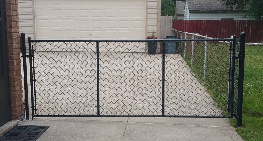 Black chain-link gate on concrete driveway in front of a garage and alongside a red fence.