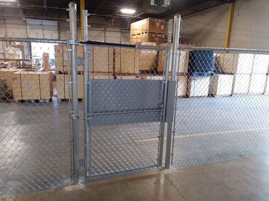 Chain link fence with a gate in a warehouse, boxes visible in the background.