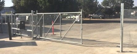 A chain-link gate is open, revealing a parking lot with a light-colored surface and several vehicles parked in the background.
