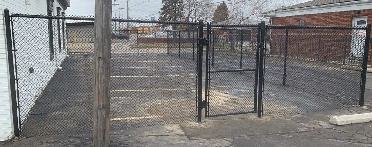 Black chain-link fence with a gate in front of a building and a parking lot.