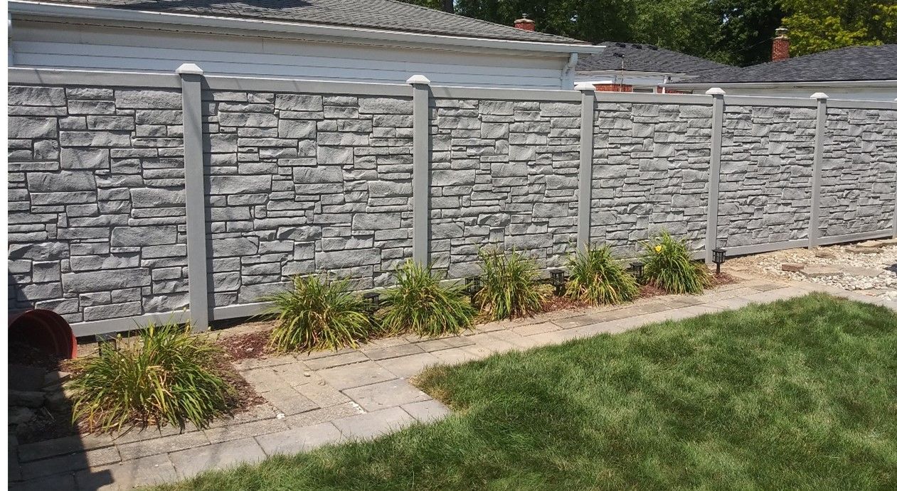 White Fence Surrounds A Lush Green Yard In Front Of A Brick House — Warren, MI — Kimberly Fence & Supply