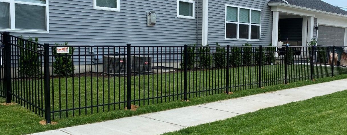 Black metal fence bordering a lawn and a sidewalk, in front of a gray house.