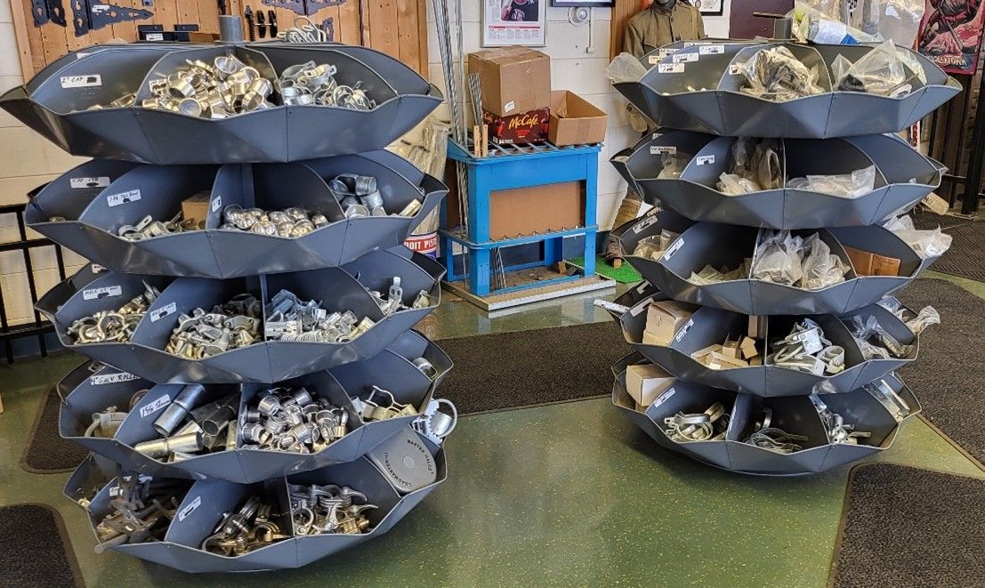 Two gray, tiered storage carousels filled with metal hardware. A cluttered workshop setting.