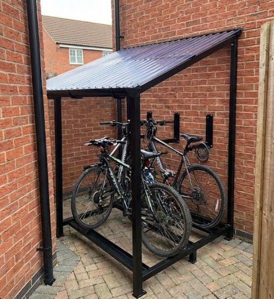 A compact lean-to bike shelter fixed against a red brick property wall, demonstrating space-efficient design for constrained locations. 