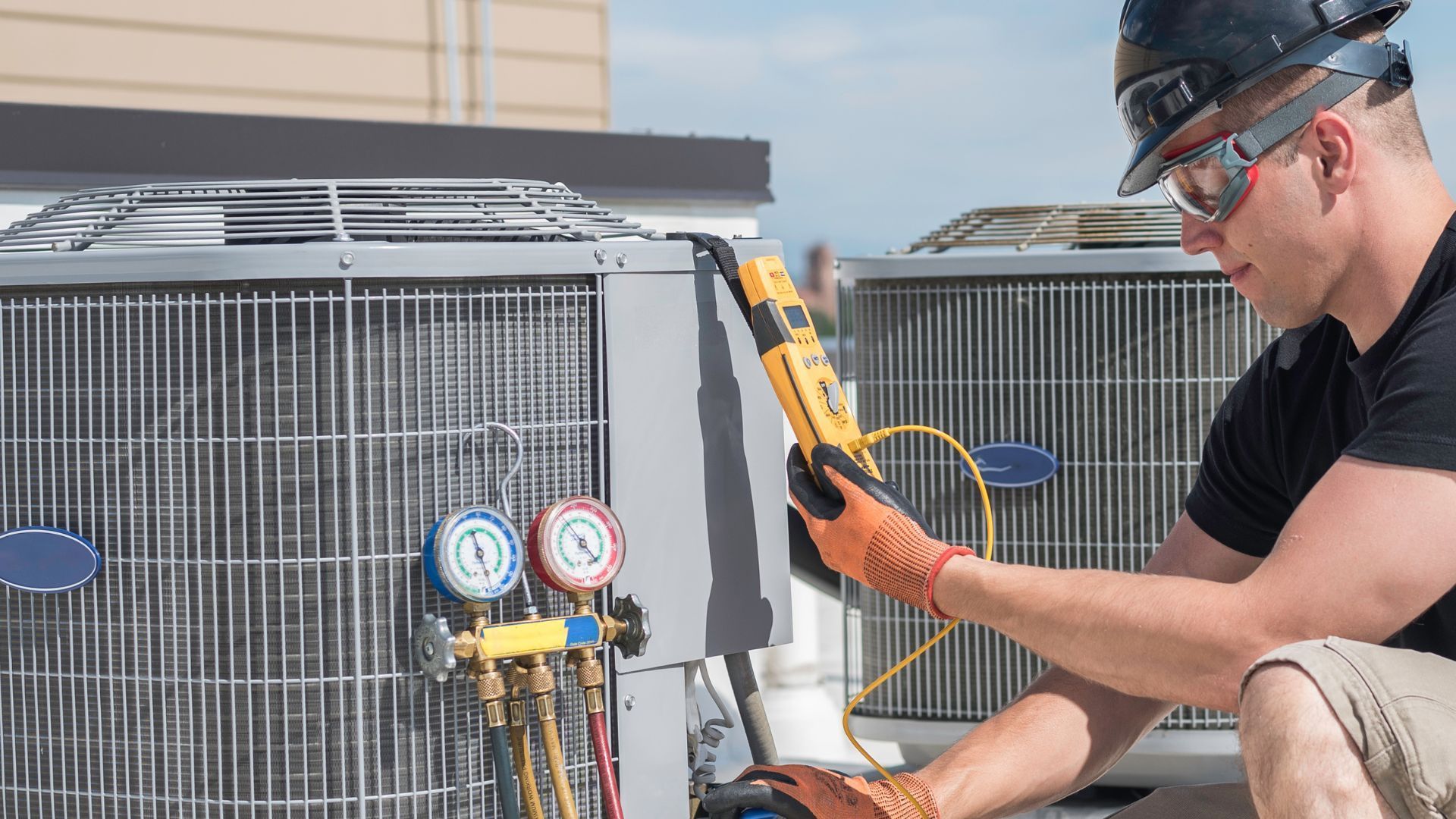 A man is working on an air conditioner on the roof of a building.