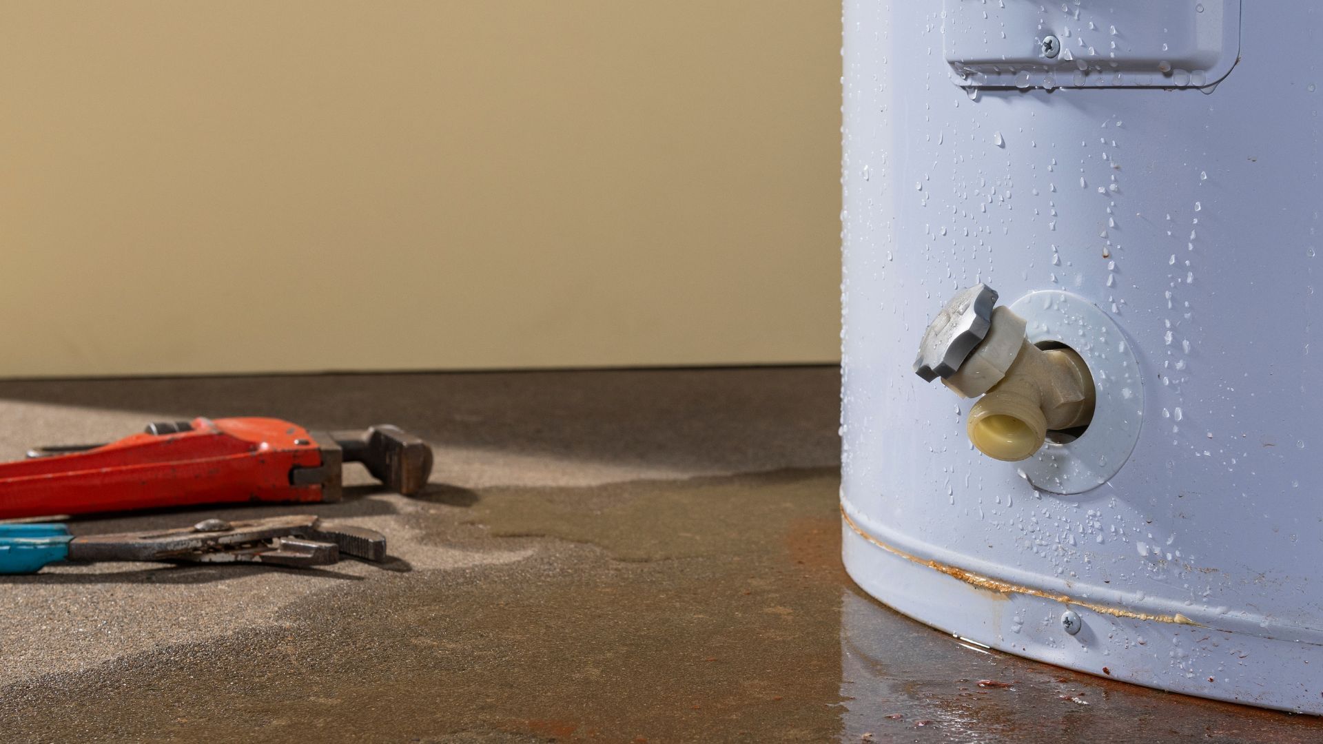 A water heater is sitting on the floor next to a wrench.