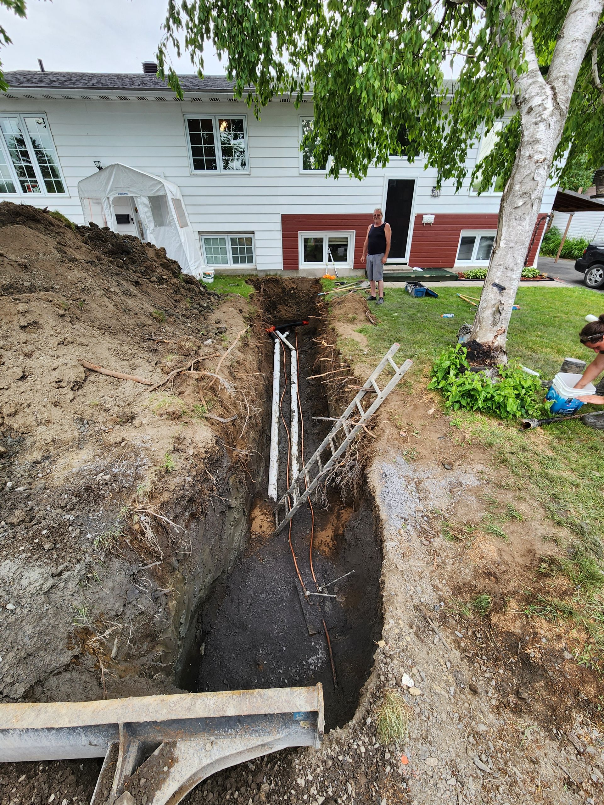 Un homme creuse un trou dans le sol devant une maison.