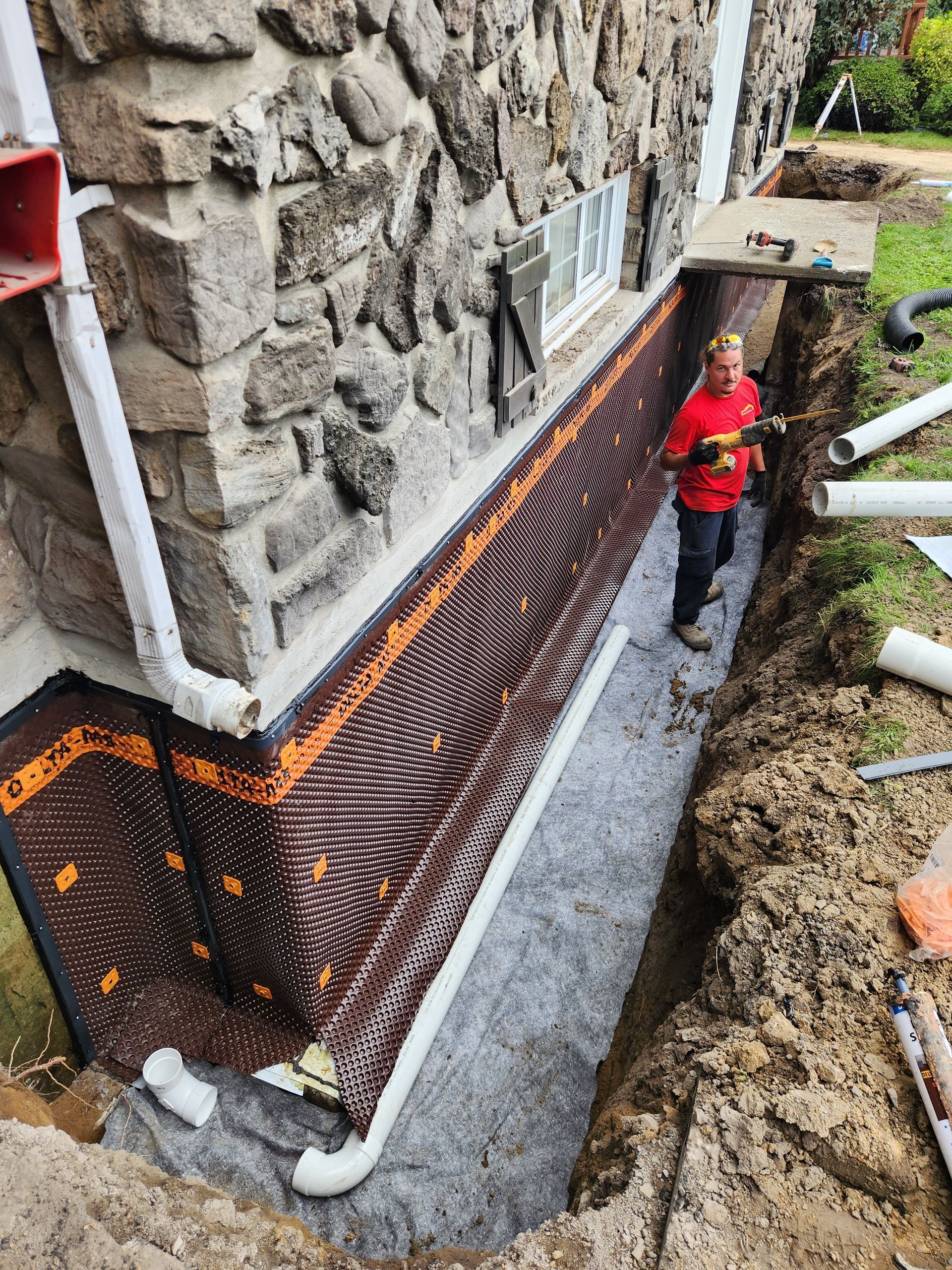 Un homme se tient dans un trou à côté d'un mur de pierre.