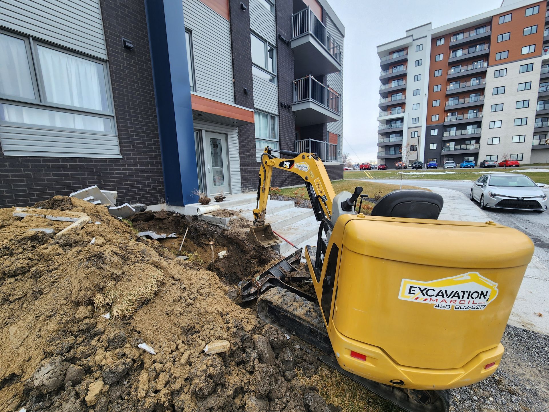 Une excavatrice jaune creuse un trou devant un bâtiment.