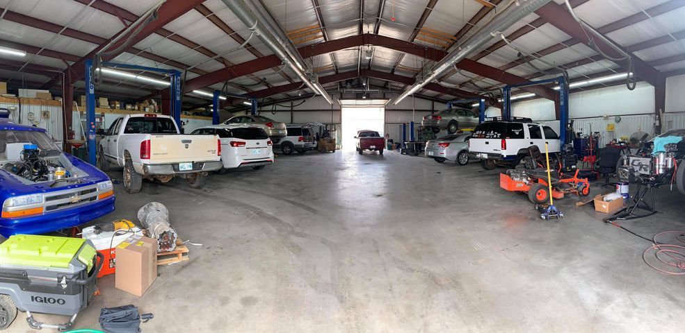 A wide shot of a garage interior with multiple vehicles in various states of repair and maintenance.