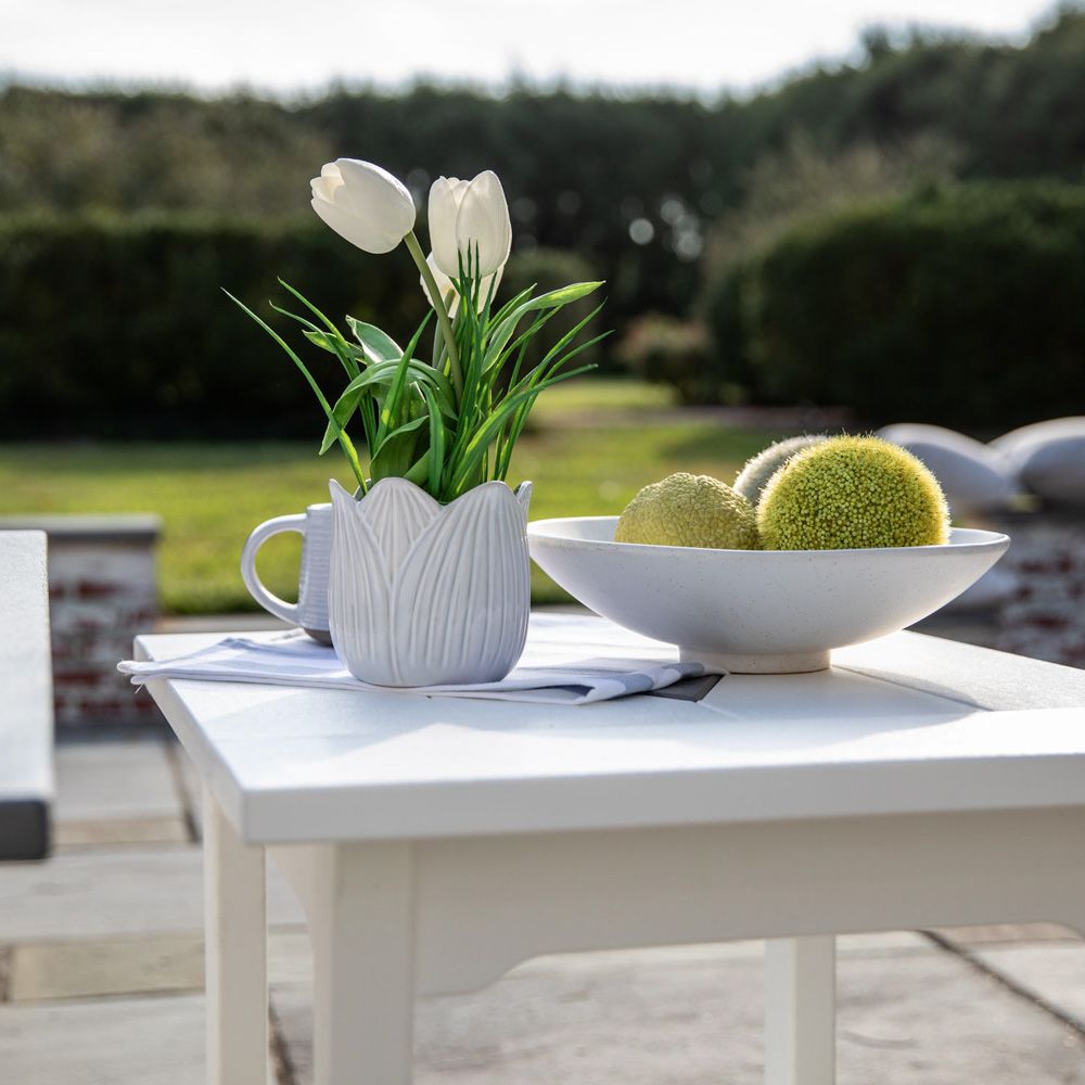 A white table with a vase of flowers and a bowl of fruit on it