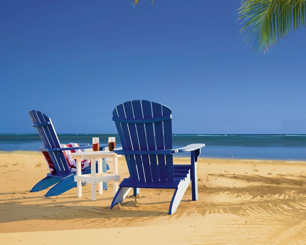Two blue and white adirondack chairs on a sandy beach