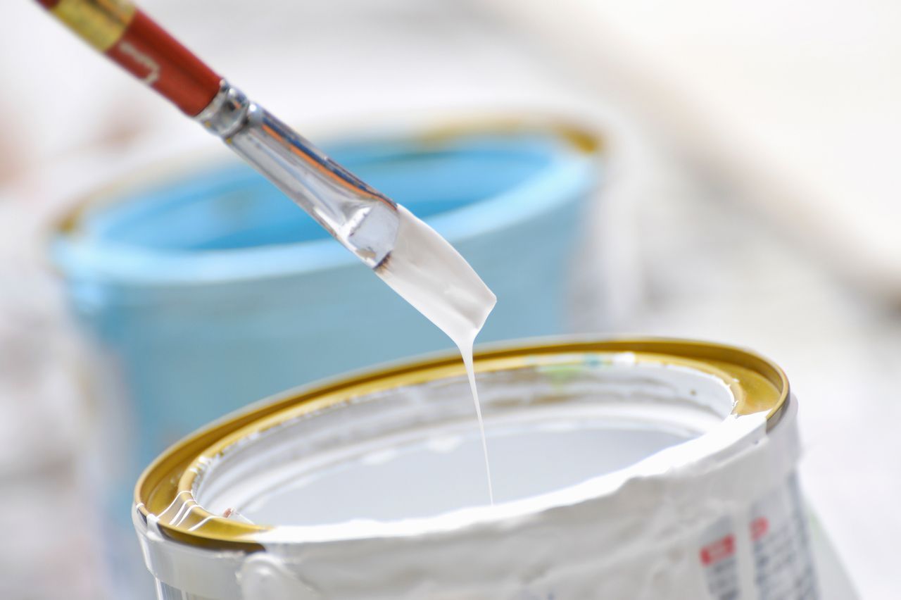 A brush is dipping into a can of white paint