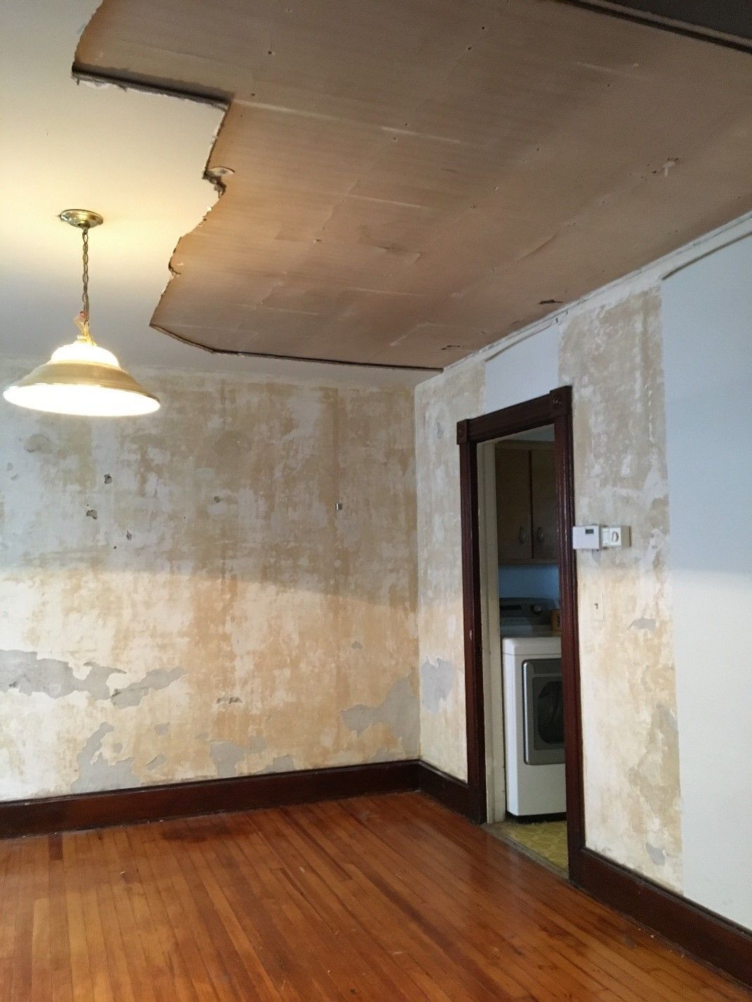 An empty room with a wooden floor and a lamp hanging from the ceiling.