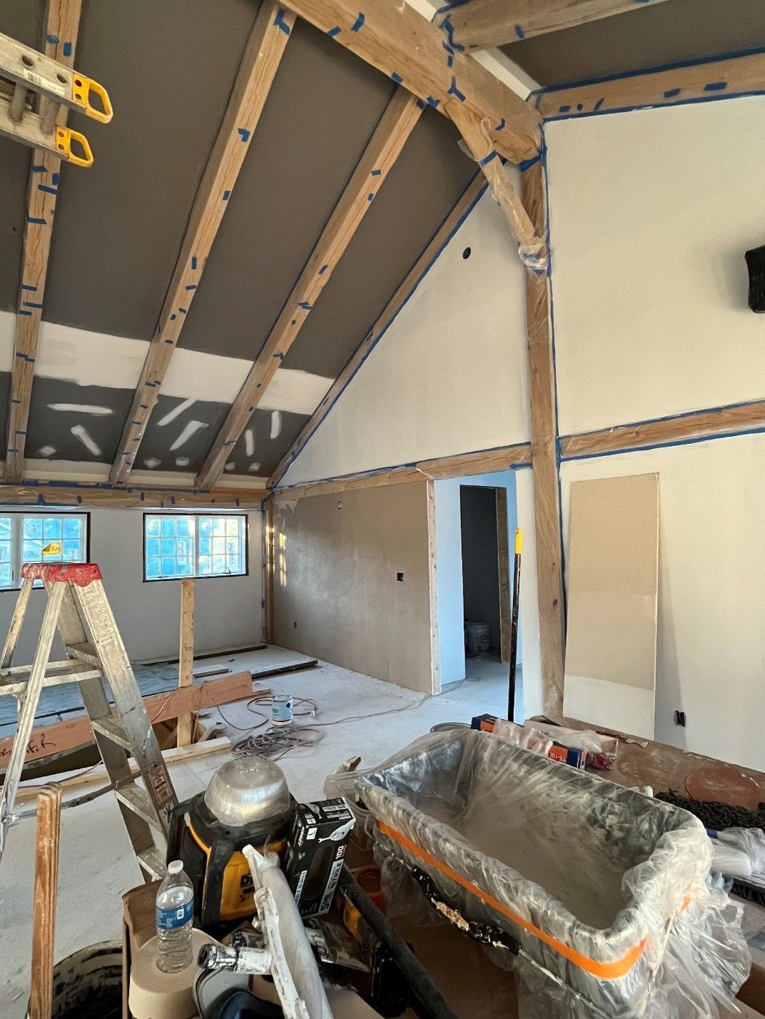 A room under construction with a ladder and a bucket of cement.