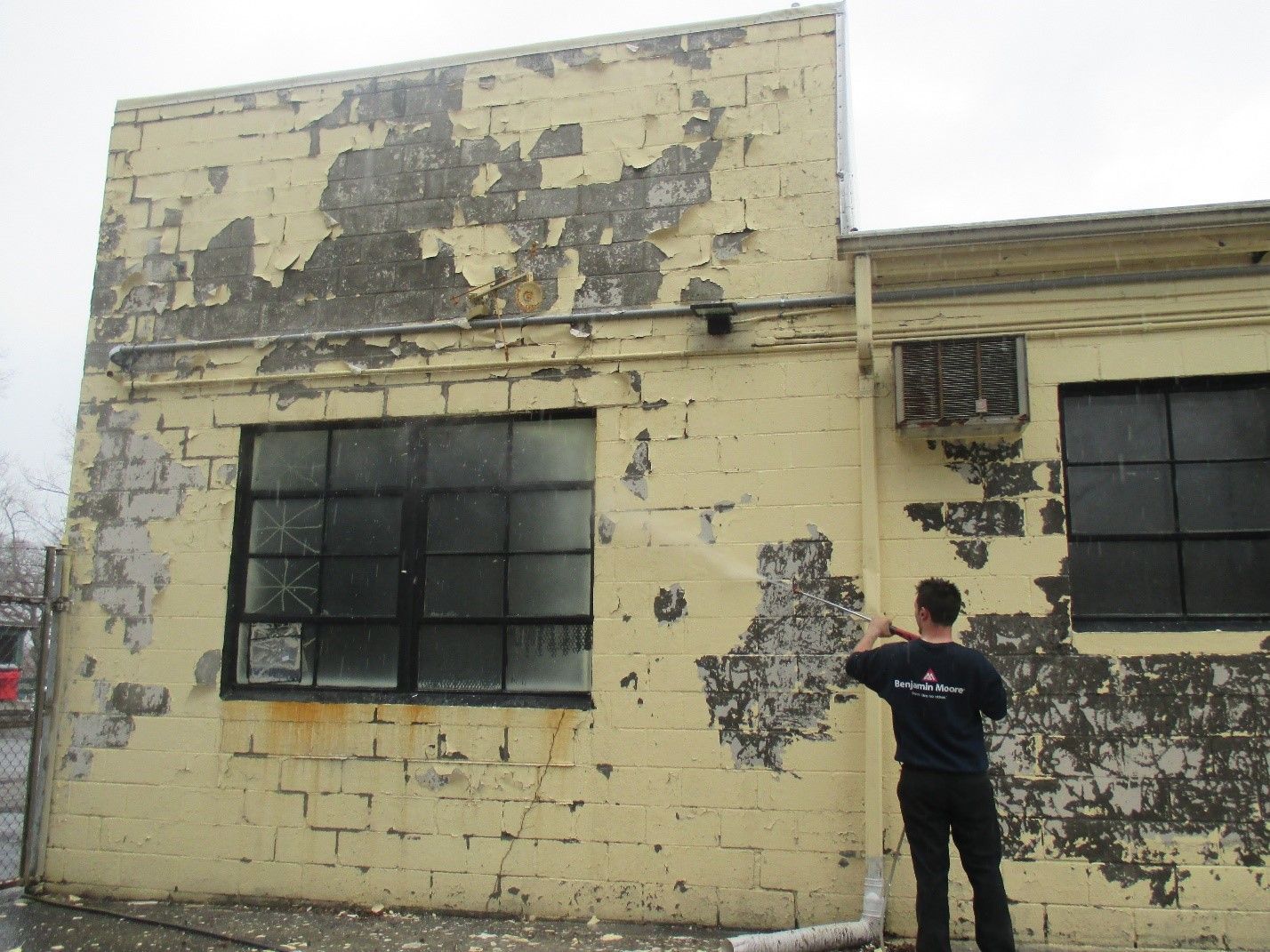 A man in a black shirt is standing in front of a yellow building