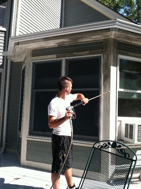 A person is cleaning a siding with a high pressure washer.