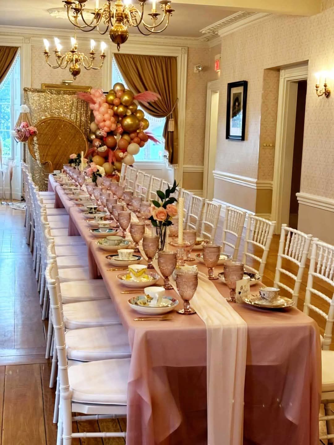 A long table with plates , glasses , candles and balloons on it.