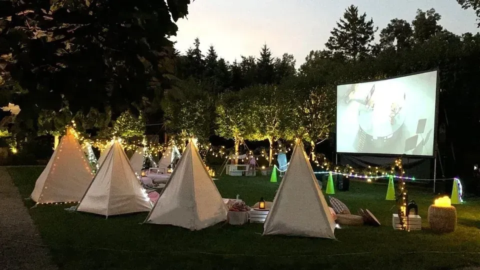 A group of tents are sitting in the grass in front of a large screen.