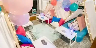 A room decorated with balloons , pillows , tables and a teepee.