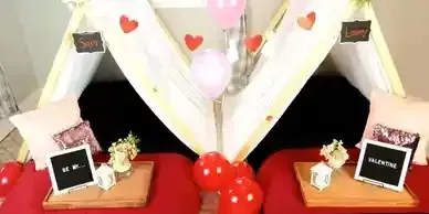 A couple of tents sitting on top of a bed with balloons and flowers.