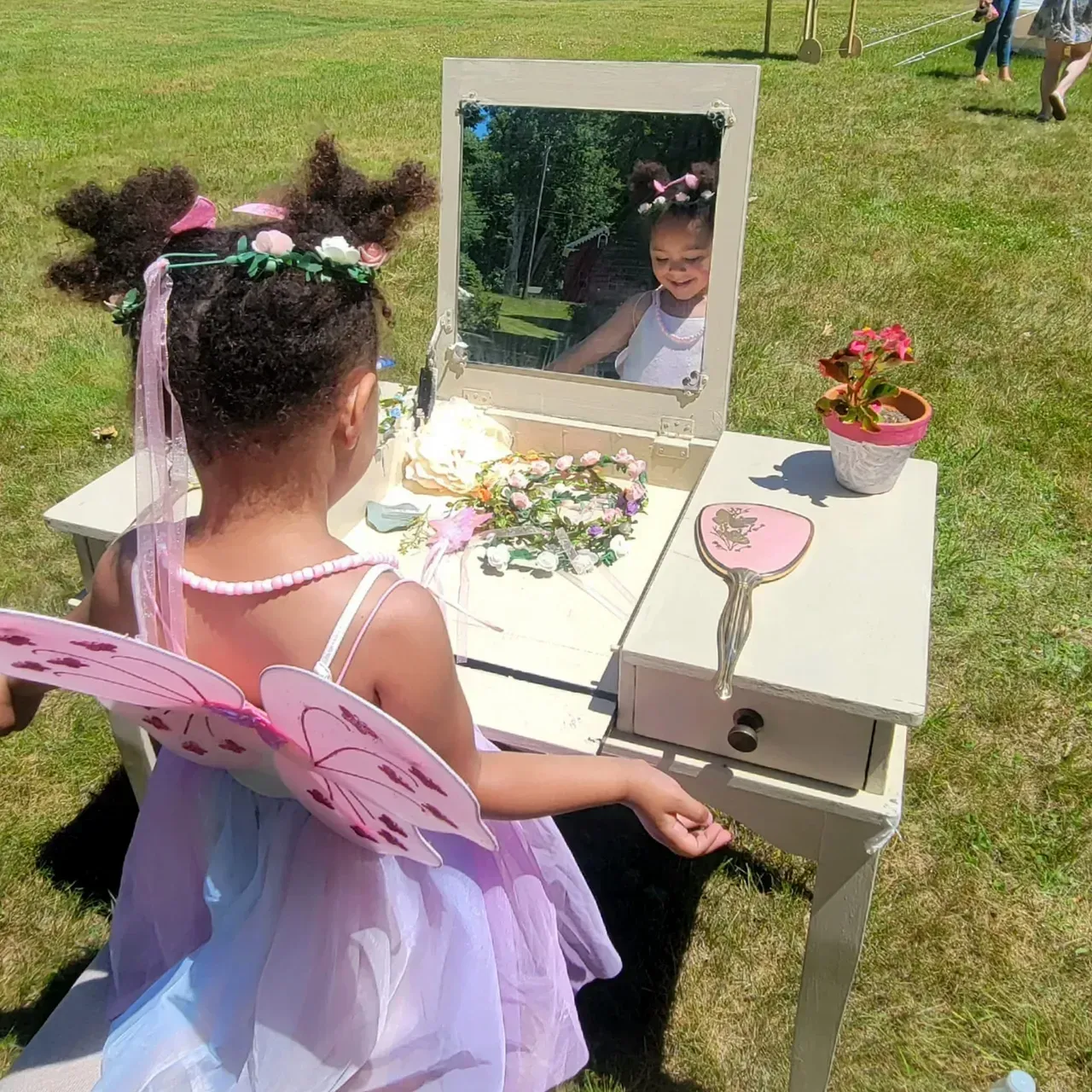 A little girl in a fairy costume is sitting at a table with a mirror.