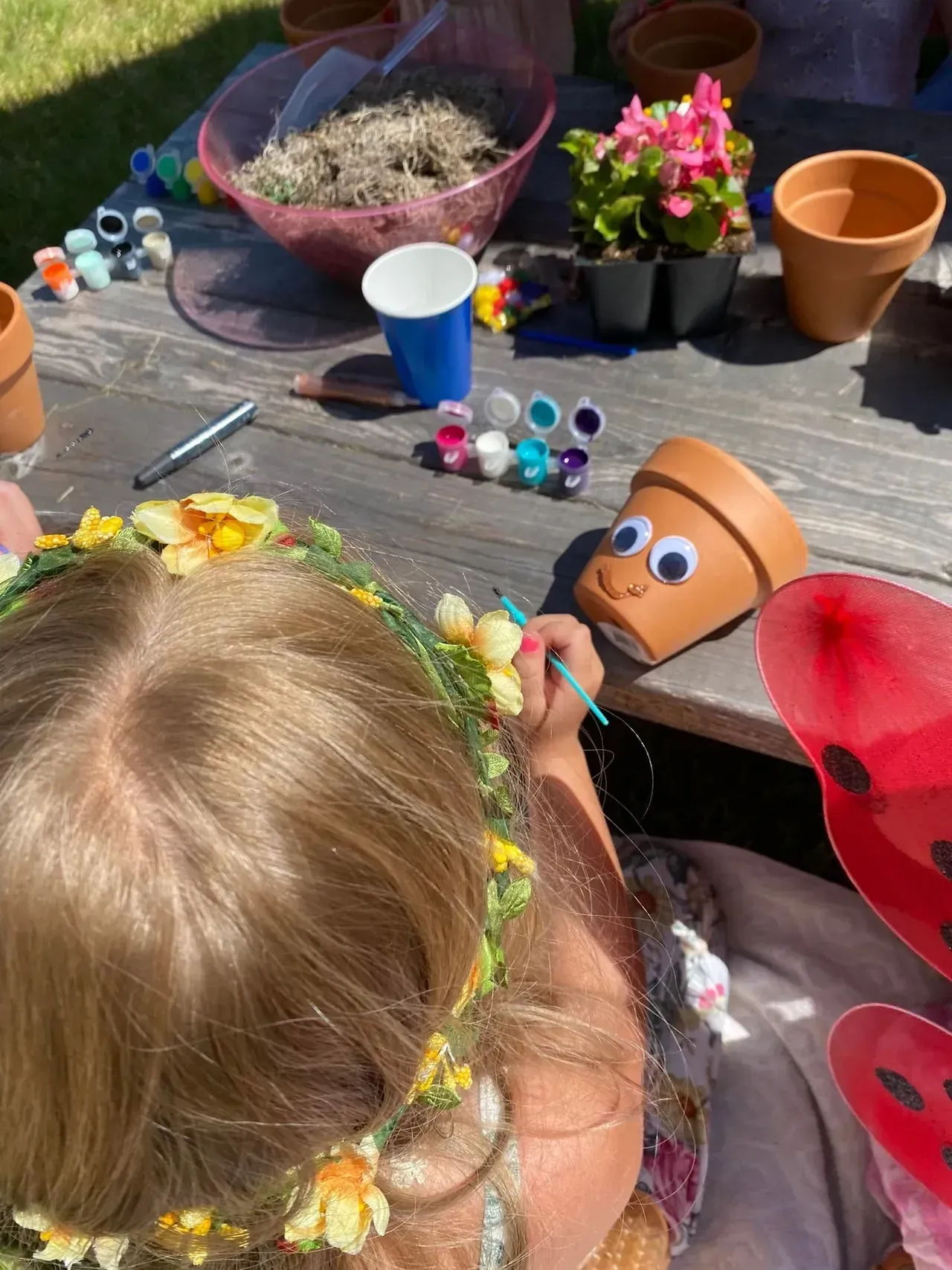 A little girl is sitting at a table painting pots with googly eyes.