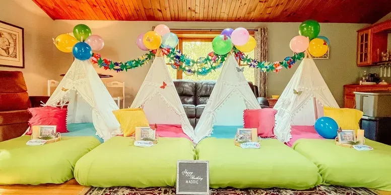 A room decorated for a sleepover with tents and balloons.