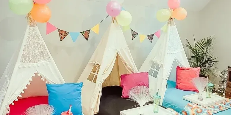 Three teepees are sitting next to each other in a room with balloons and pillows.
