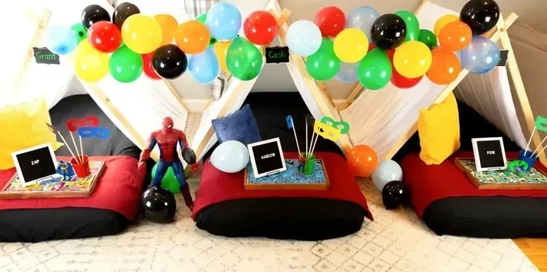 A spiderman figure is sitting on a pillow in front of a tent with balloons.